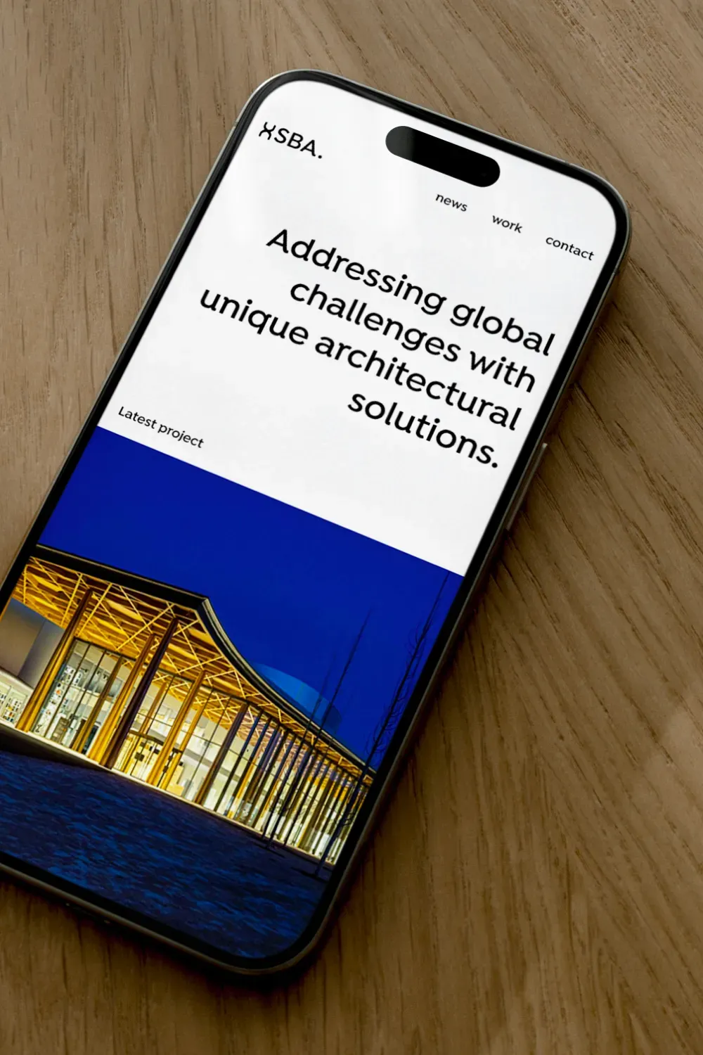 Smartphone posé sur bois affichant le site web SBA, page d'accueil architecture avec projet de bâtiment illuminé la nuit