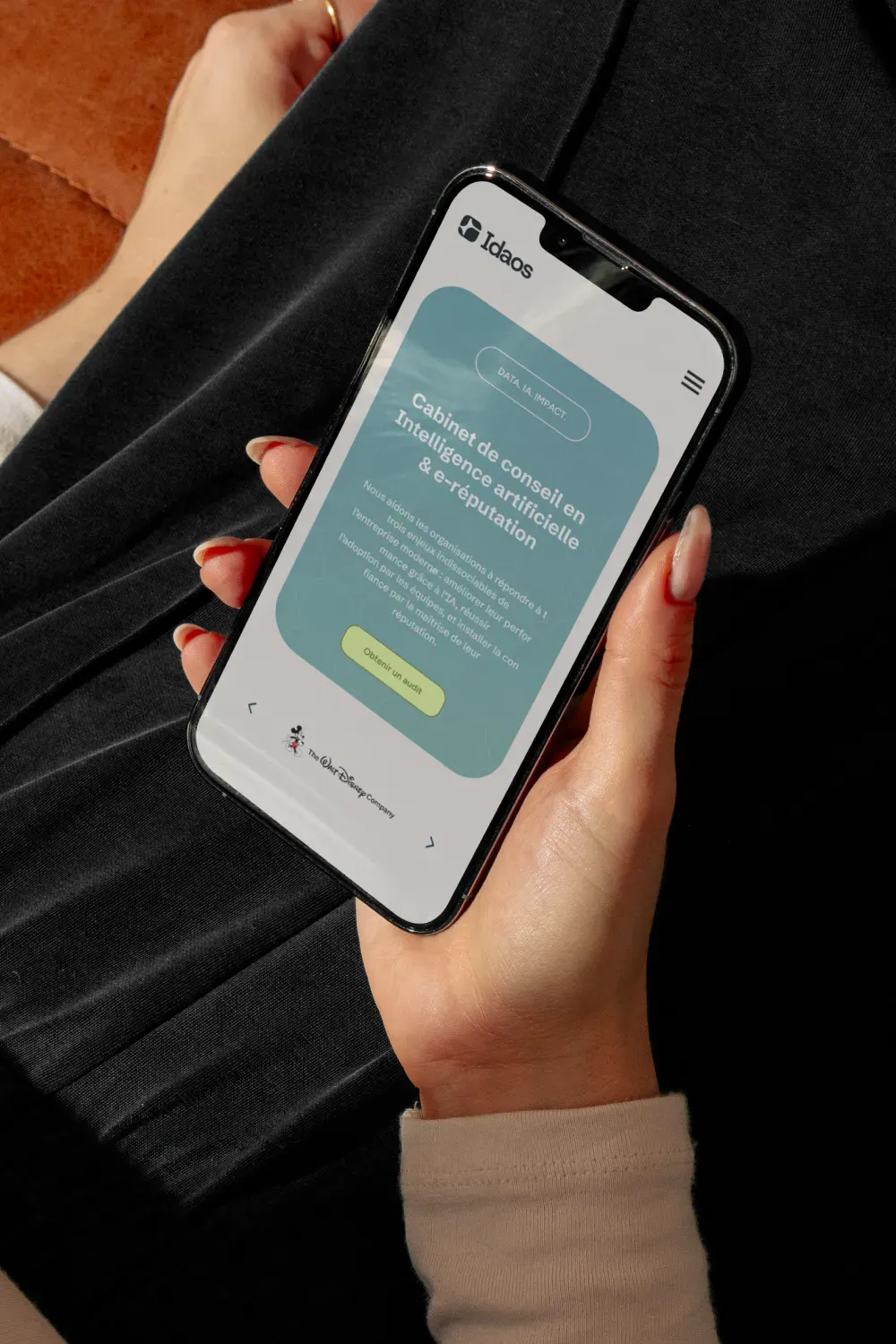 Main tenant un smartphone affichant la version mobile du site Idaos, page d'accueil cabinet de conseil en intelligence artificielle